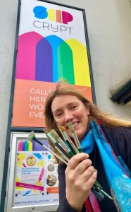 Alicia Tolhurst-Brown holding a range of paint brushes outside the Crypt Gallery Seaford